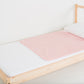 Pink medium-sized PeapodMat waterproof bedding protector lying on a single bed.